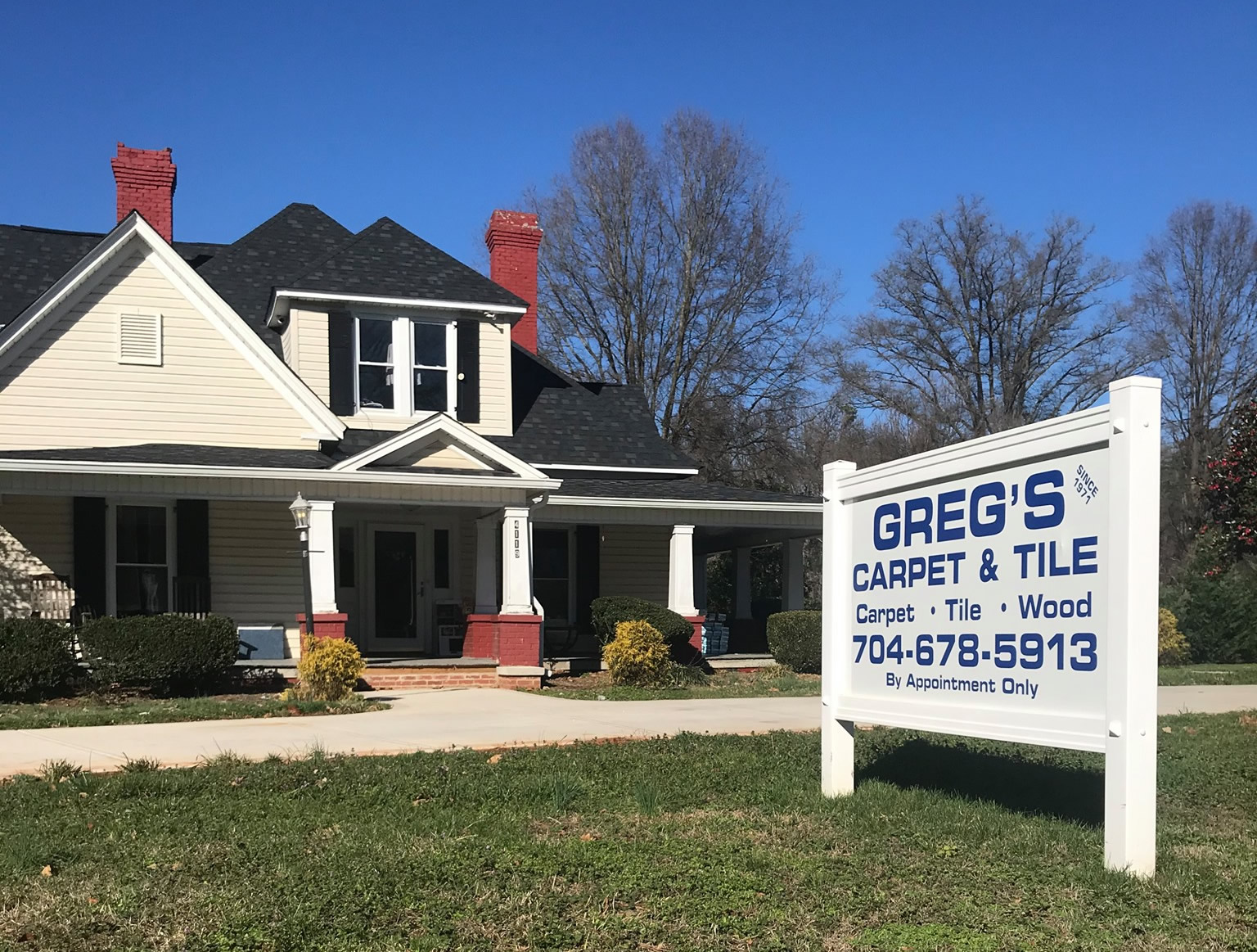 A sign in front of a house with trees and bushes.