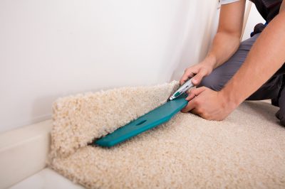 A person using a blue carpet cutter to cut the carpet.